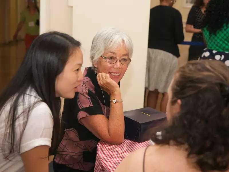 一位年长的校友认真地听两位年轻的女士讲话